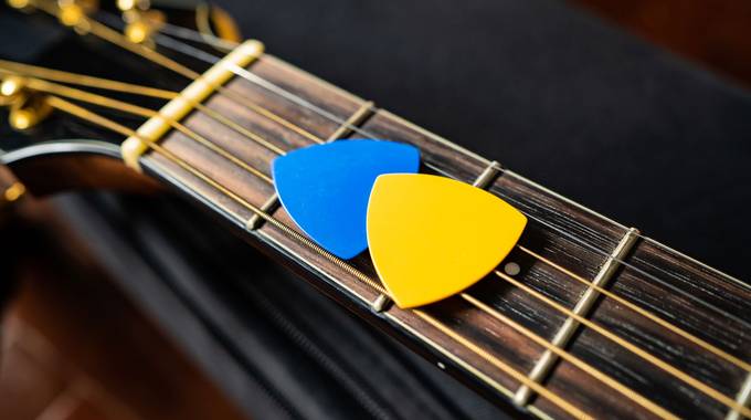 Plektrons in Gelb und Blau liegen auf einer Gitarre