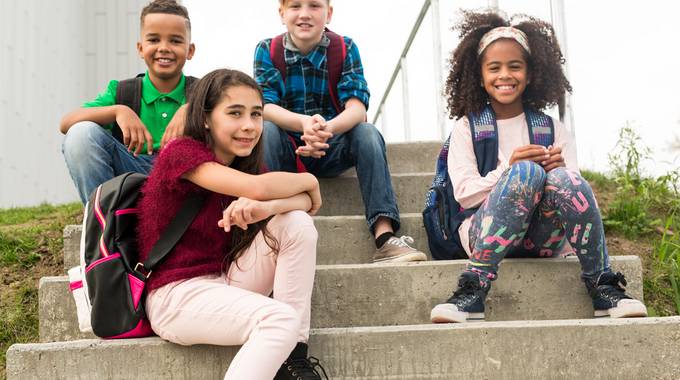 Vier Kinder sitzen auf einer Schultreppe und schauen nach vorne