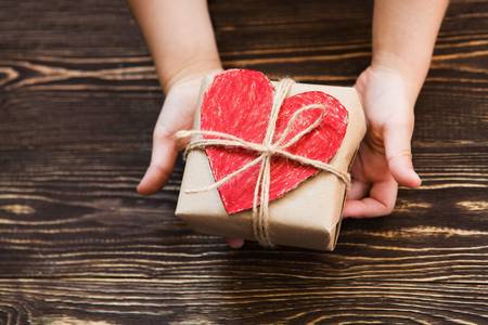 Eine Kinderhand hält ein Paket mit einem roten Herzen