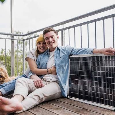 Ein junges Paar sitzt auf dem Balkon neben einem Steckersolargerät