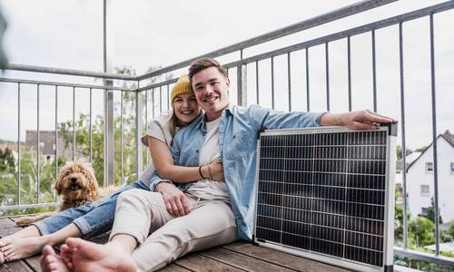 Ein junges Paar sitzt auf dem Balkon neben einem Steckersolargerät